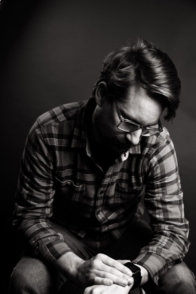 black and white image of man looking at watch with glasses and beard wearing a flannel shirt