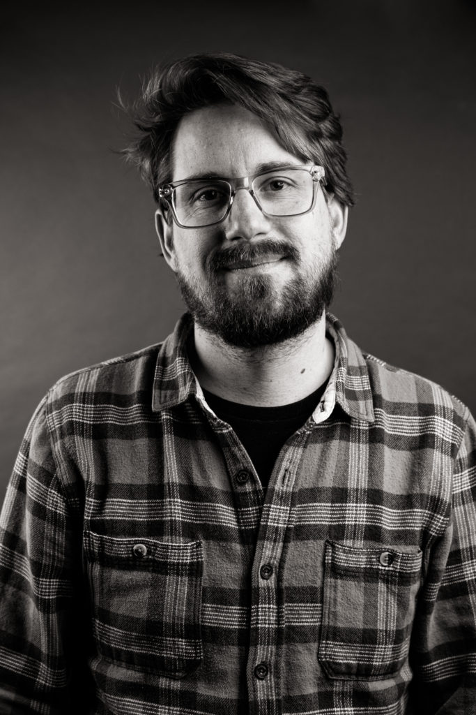 black and white image of man with glasses and beard wearing a flannel shirt