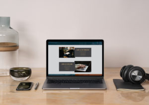 open laptop, iphone, and headphones displayed on a wood desk with a white wall in the background