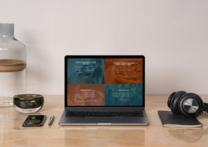 open laptop, iphone, and headphones displayed on a wood desk with a white wall in the background